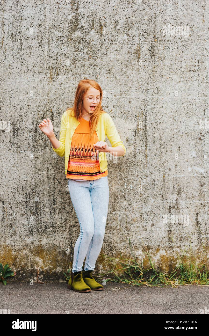 Outdoor portrait of pretty little girl with red hair, wearing orange t-shirt and yellow jacket Stock Photo