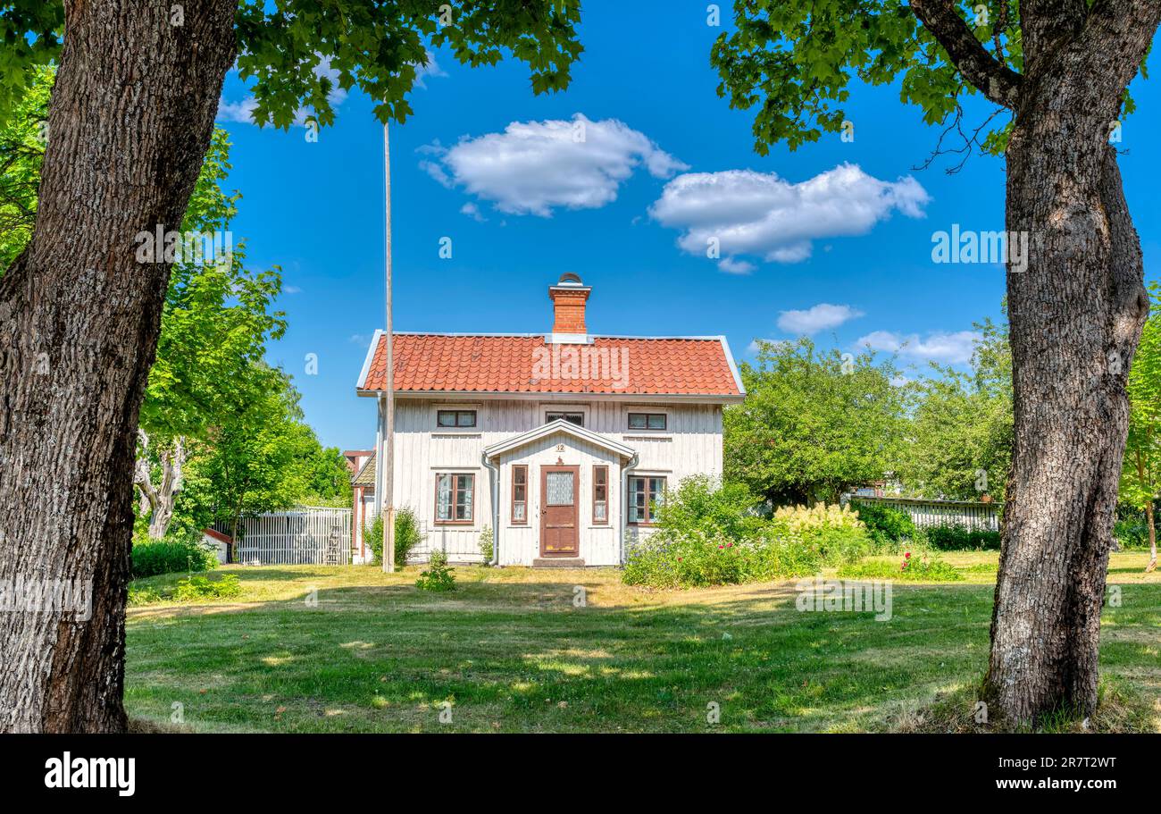 Traditional Swedish wooden house with red tiled roof surrounded by green trees under a bright blue summer sky, Sweden. Stock Photo