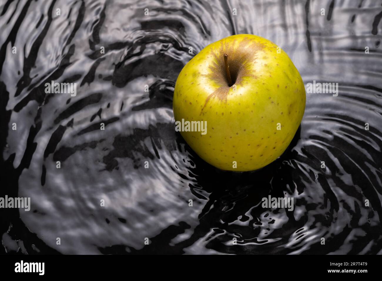 Yellow apple falling into the water with waves around it black background and copy space Stock Photo