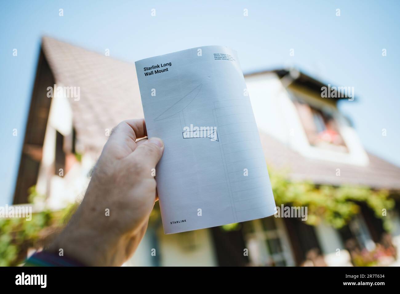 Germany - Jun 16, 2023: Male hand holding new Starlink Wall Mount insutrction manual in hand with his house in background - ready to install de intern Stock Photo