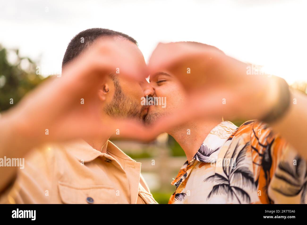 Portrait of gay boyfriend and girlfriend making the heart or love gesture kissing at sunset in a park in the city. Diversity and lgbt concept Stock Photo