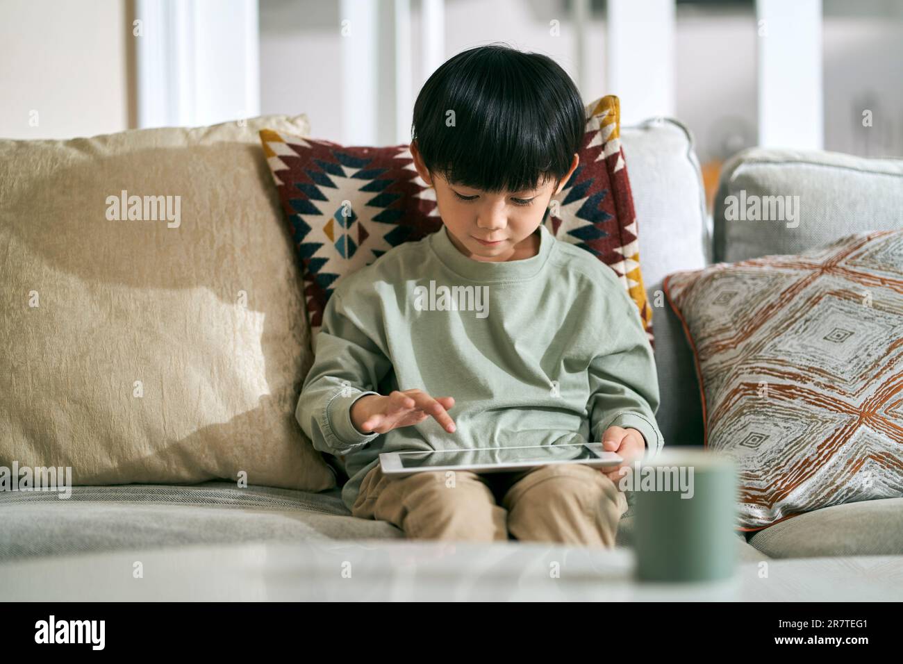 fiveyearold little asian boy sitting on family couch at home using