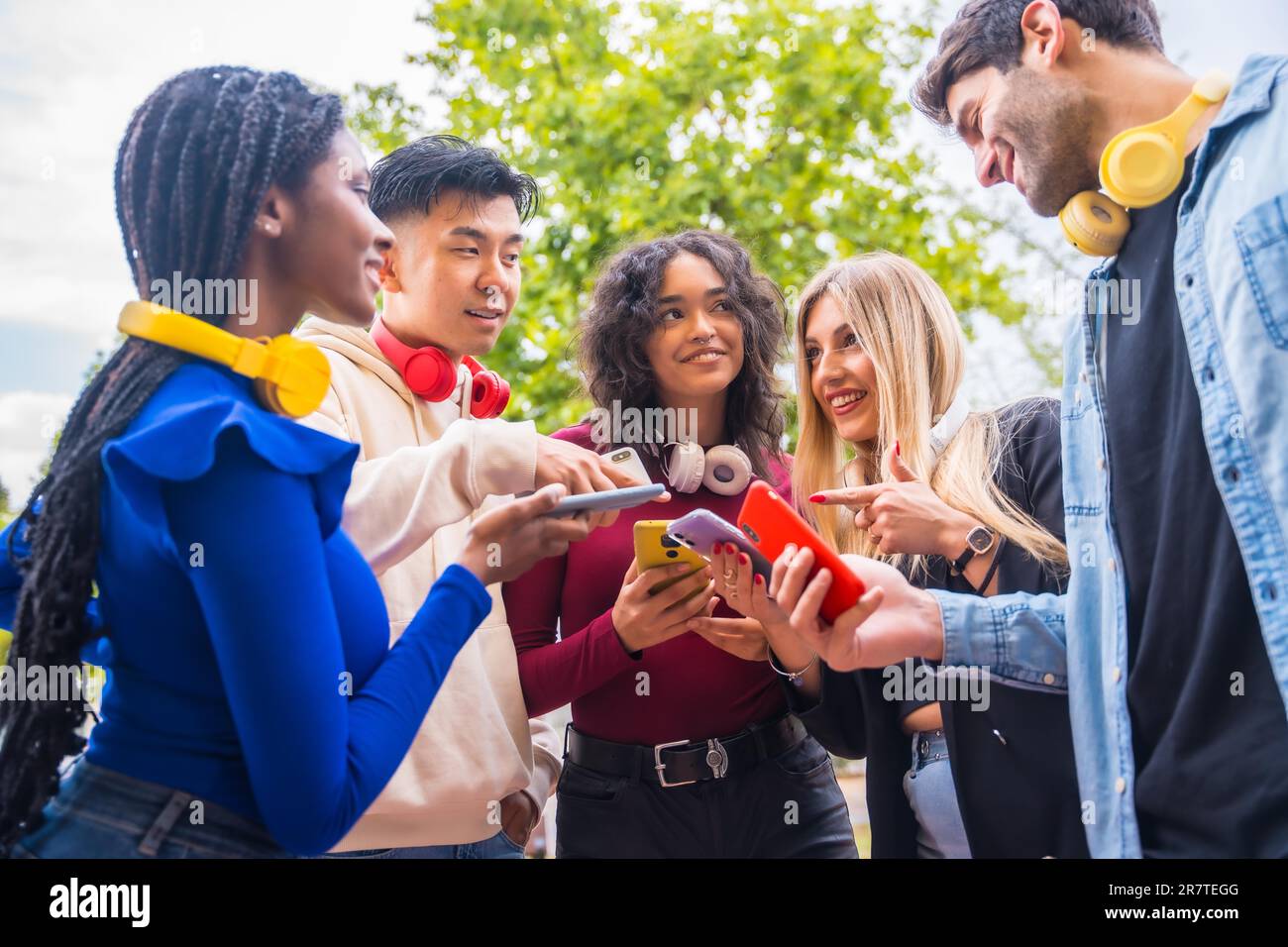 Group of young smiling teenage multiethnic friends using cell phones on ...