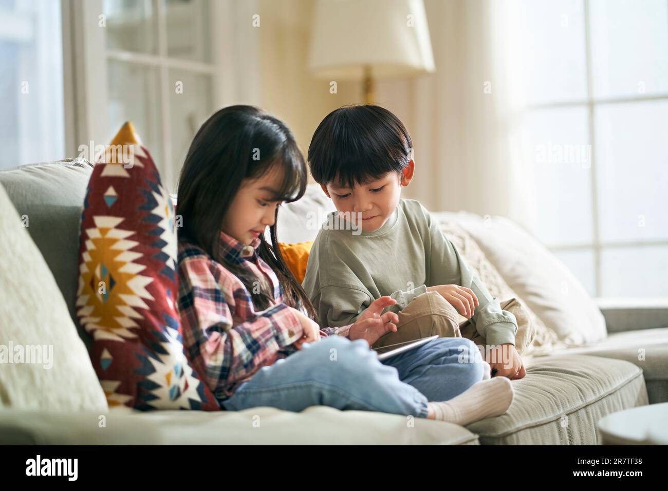 little asian children brother and sister sitting on family couch at home using digital tablet computer together Stock Photo
