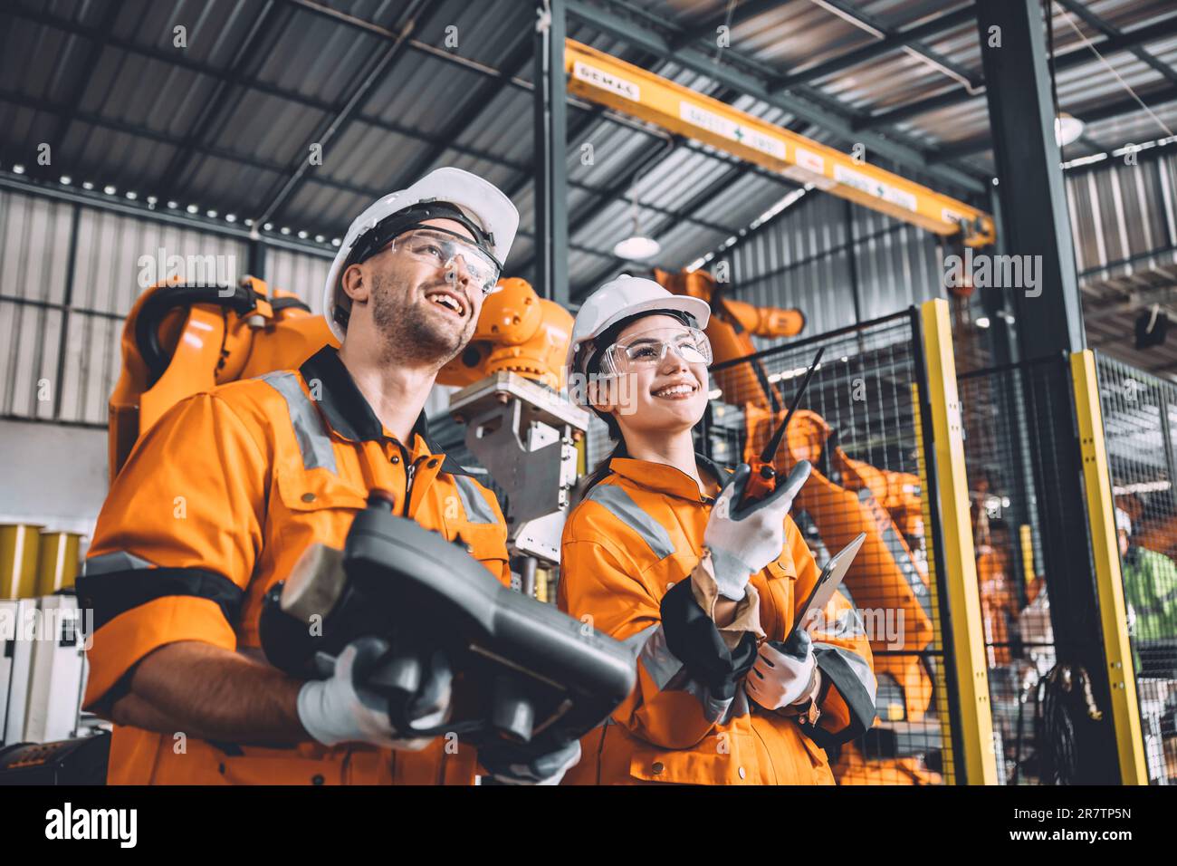 Engineer team working with robot welding in automation factory. People worker in safety suit control robotic arm in automated manufacturing industry t Stock Photo