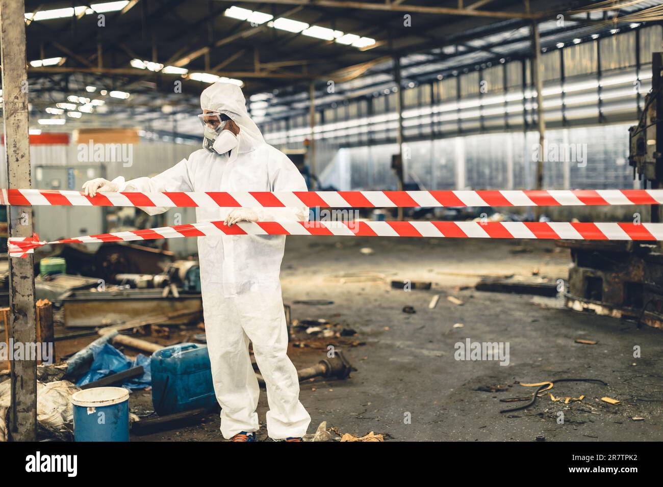 Worker in PPE safety suit with area closed barricade security tape in danger dirty area from virus infected chemical leak Stock Photo