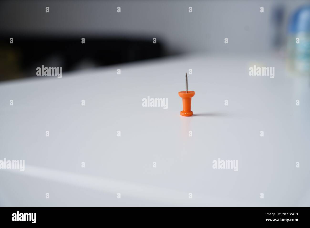 One orange pin stands alone on a white background table with space for