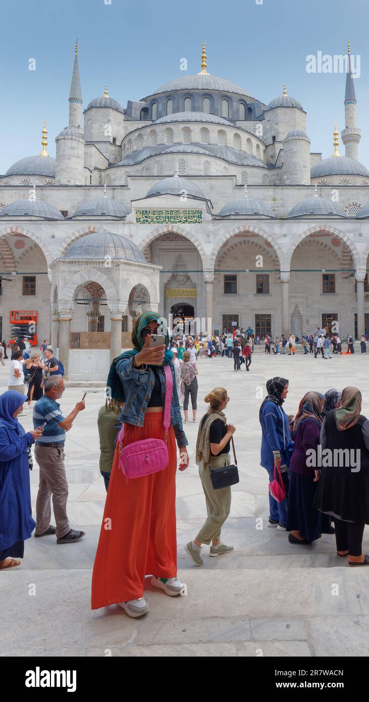 Woman wearing an orange skirt, denim jacket and hijab takes a selfie in the courtyard of the Sultan Ahmed Mosque aka Blue Mosque. Istanbul, Turkey Stock Photo