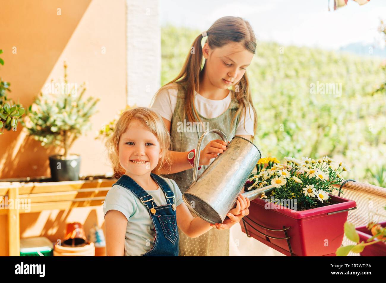 Group of two children watering flowers on balcony, young girl help with small home garden Stock Photo