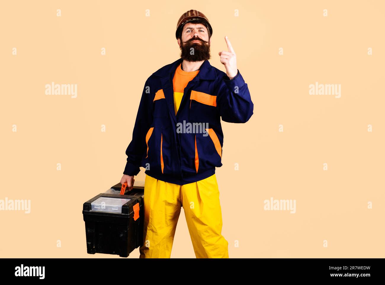 Service man in workwear with toolbox. Repairman with tool box pointing finger up. Repair. Handyman, workman in uniform with repair kit. Builder in Stock Photo