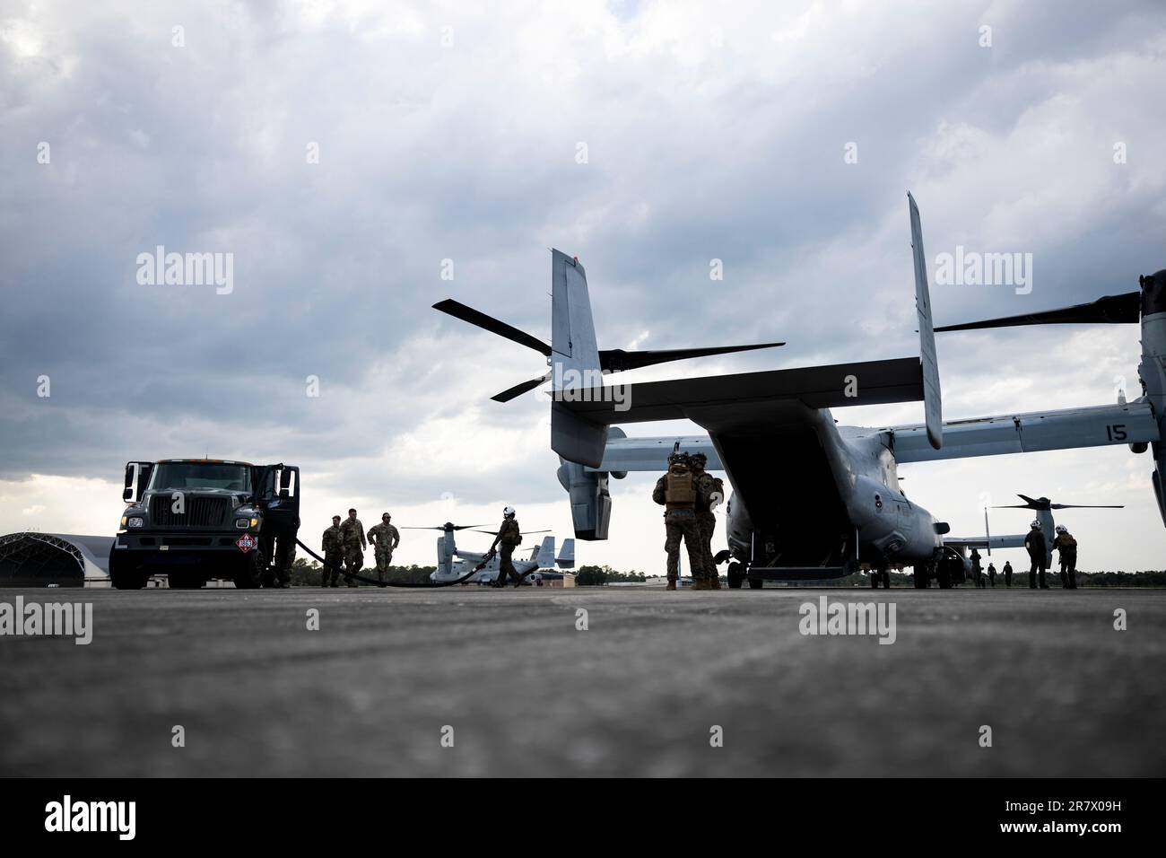 U.S. Marine Corps MV-22 Osprey is refueled by U.S. Airmen after a simulated High Mobility Artillery Rocket System (HIMARS) fire, Avon Park Air Force Range, Florida, May 30, 2023. The tanker truck was carried in a U.S. Air Force C-17 Globemaster III’s cargo hold as part of a new strategy of carrying fuel that is used for several aircraft before being loaded back on the C-17. Once all the aircraft were refueled, the remaining fuel was drained into the C-17 fuel tank before the empty tanker truck was loaded back onto the aircraft as part of a new refueling sustainability concept. The simulated fi Stock Photo