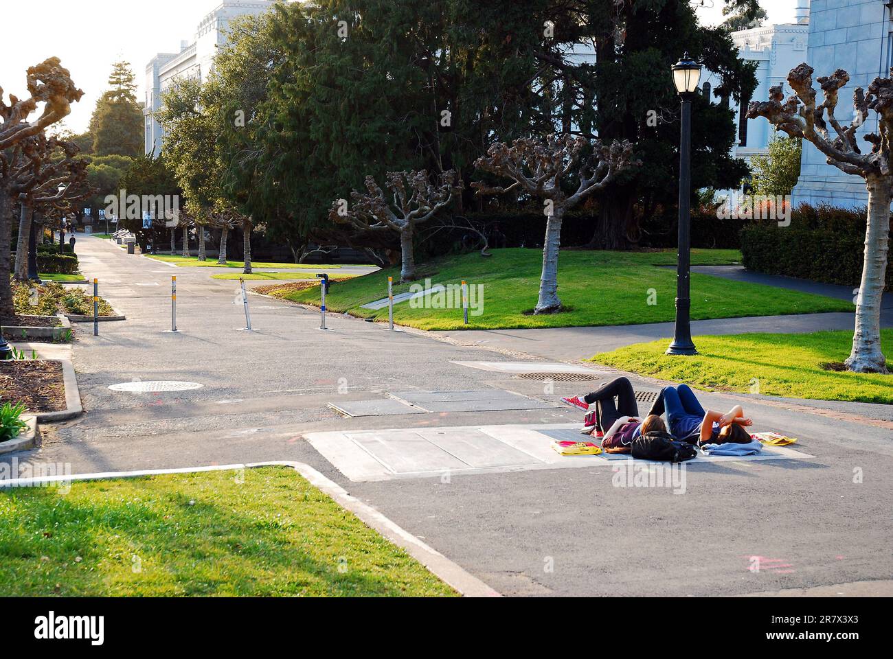 Two students lay on a footpath to watch the sunset from the campus of the University of California, Berkeley Stock Photo