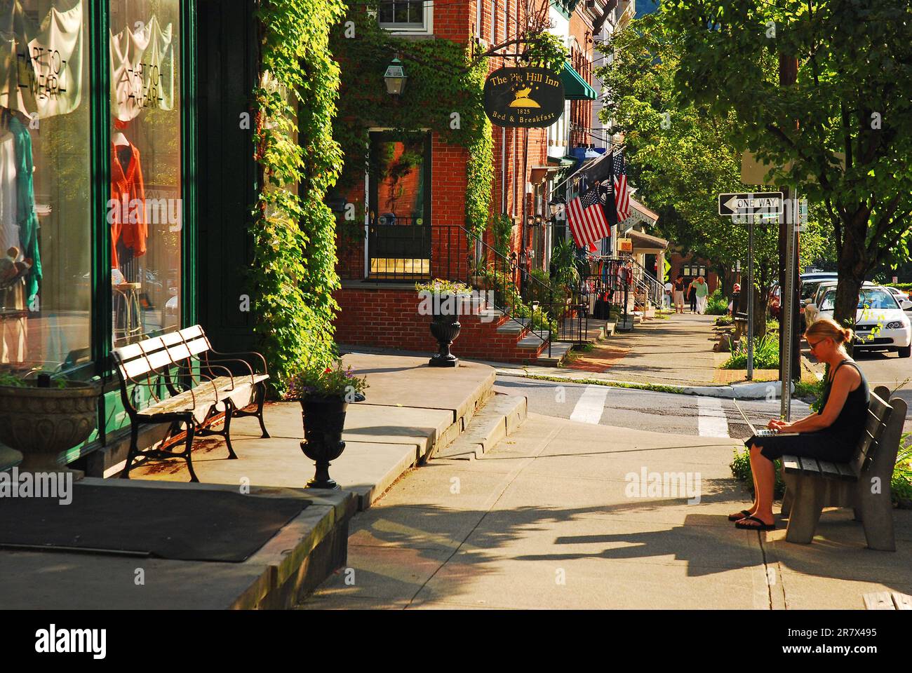 A young woman works on a laptop while sitting on a bench in the downtown business district of a small town instead of the office Stock Photo