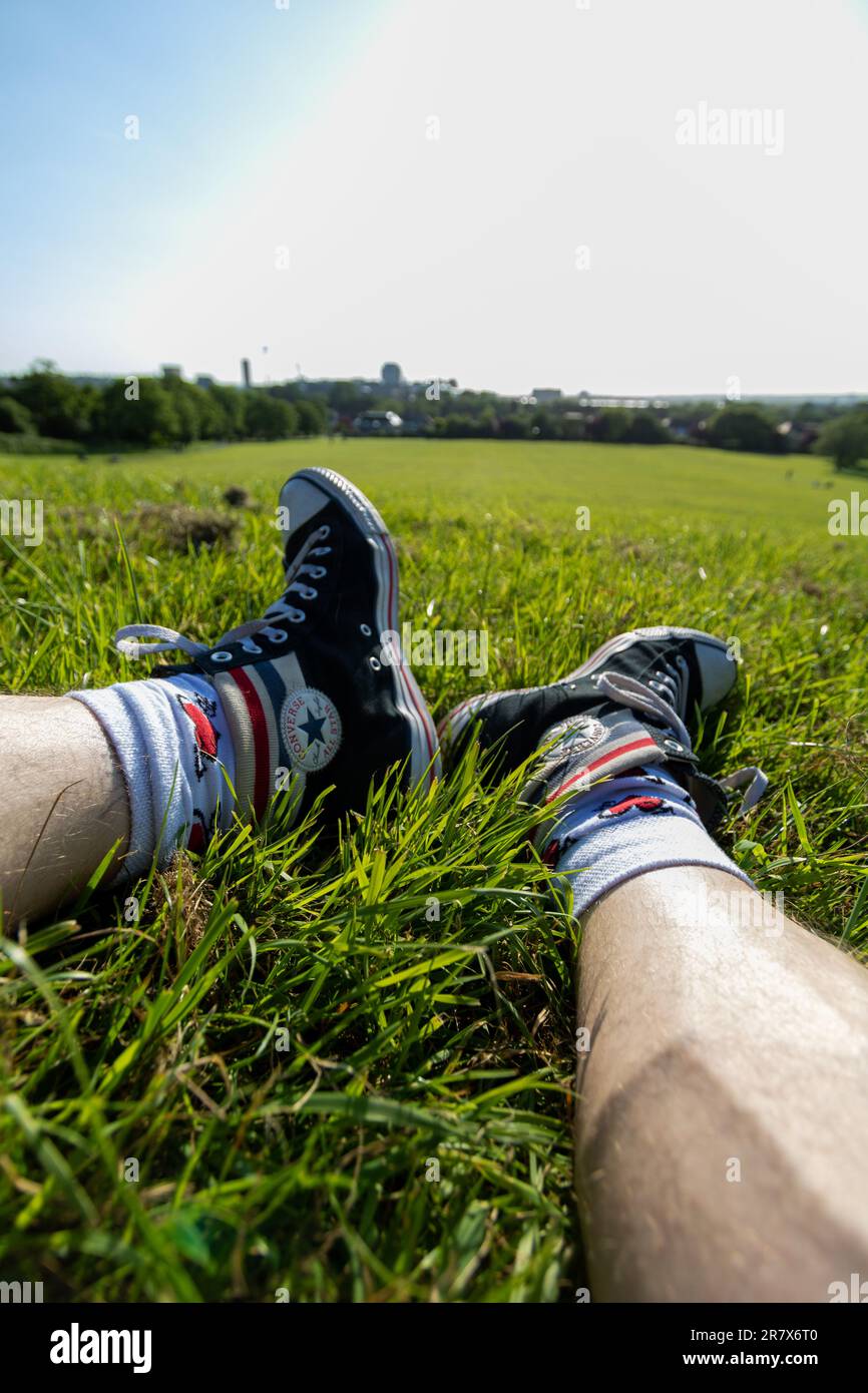 Legs on the grass wearing Convers shoes and long socks with a heart pattern. Cityscape skyline on a sunny summer day in the park. Stock Photo