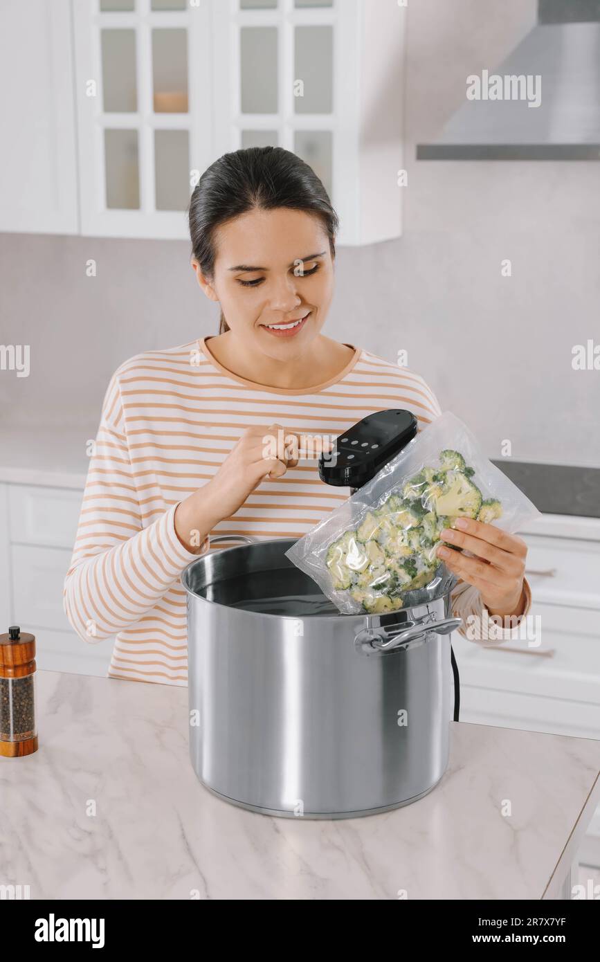 Woman putting vacuum packed broccoli into pot and using thermal immersion circulator. Sous vide