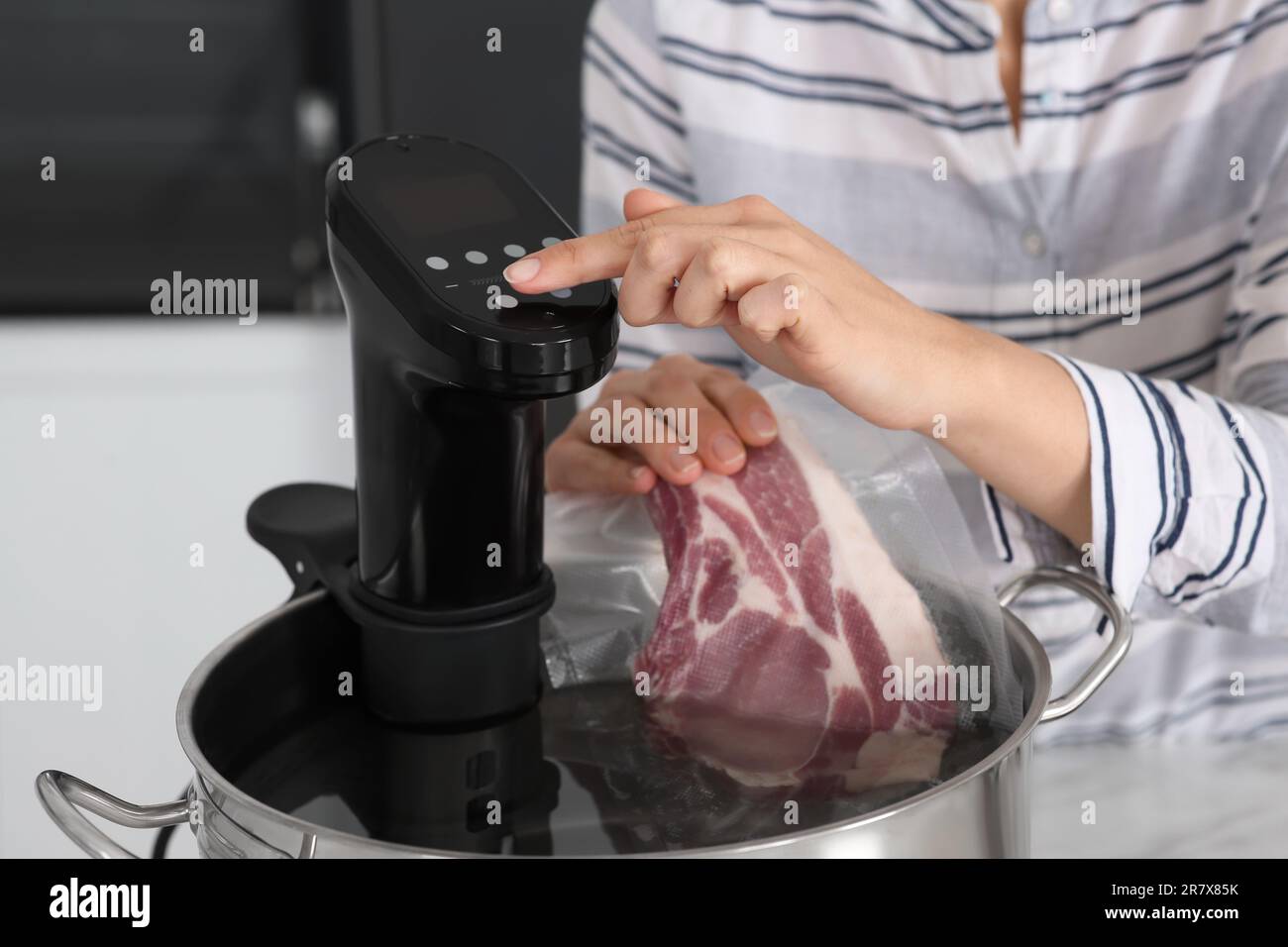 Woman putting vacuum packed meat into pot and using thermal immersion