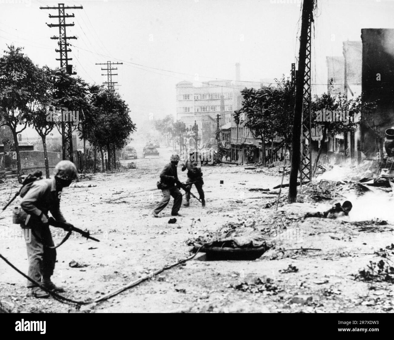 U.S. Marines engaged in street fighting during the liberation of Seoul. Note M-1 rifles and Browning Automatic Rifles carried by the Marines, dead Koreans in the street, and M-4 'Sherman' tanks in the distance. Stock Photo