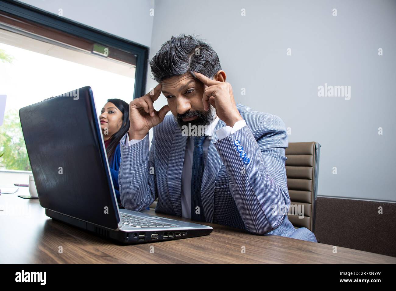 Stressed and exhausted young indian businessman sit in office working on laptop massage temples suffer from headache.Tired unhealthy male employee str Stock Photo