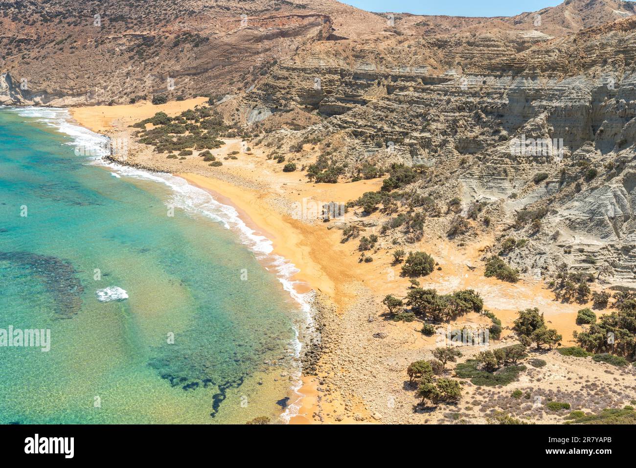 Potamos bay with the long reddish beach and shallow water, formed at the exit of a small canyon with majestic geological clay formations and steep Stock Photo