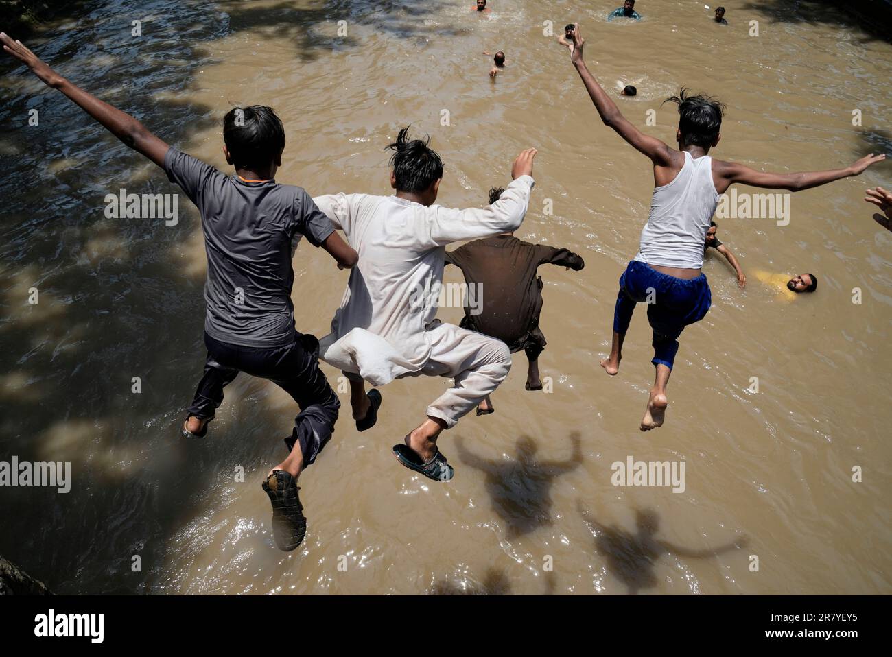 Pakistani youths jump into the water as they and others swim in a canal