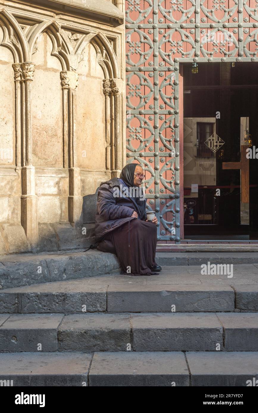 An old Grandma is sitting in front of the church Santa Maria del Mar in Barcelona. Poor people in front of churches must beg for small money. Plenty Stock Photo
