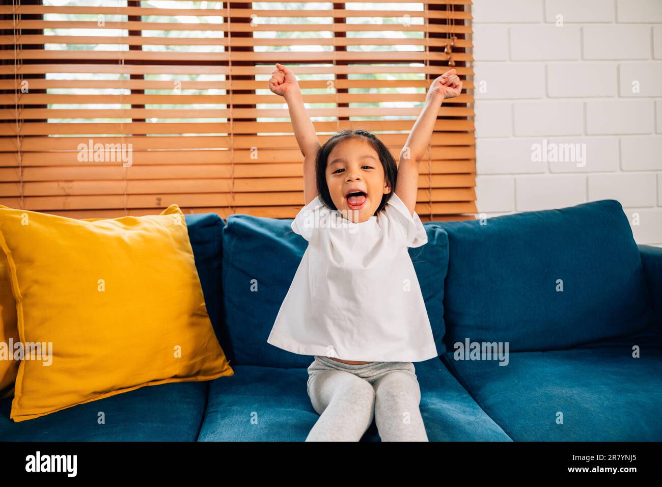 Happy cute girl with hands up sitting on comfortable sofa Stock Photo ...