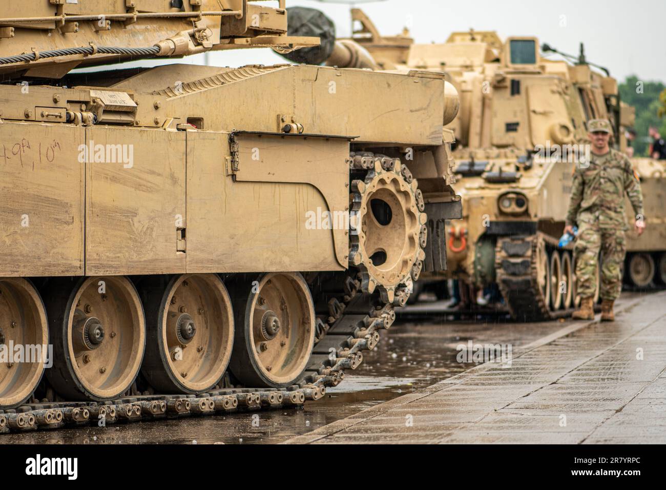 American United States Marine Corps soldier walking under the rain near moving Abrams armoured tanks, NATO response force Stock Photo