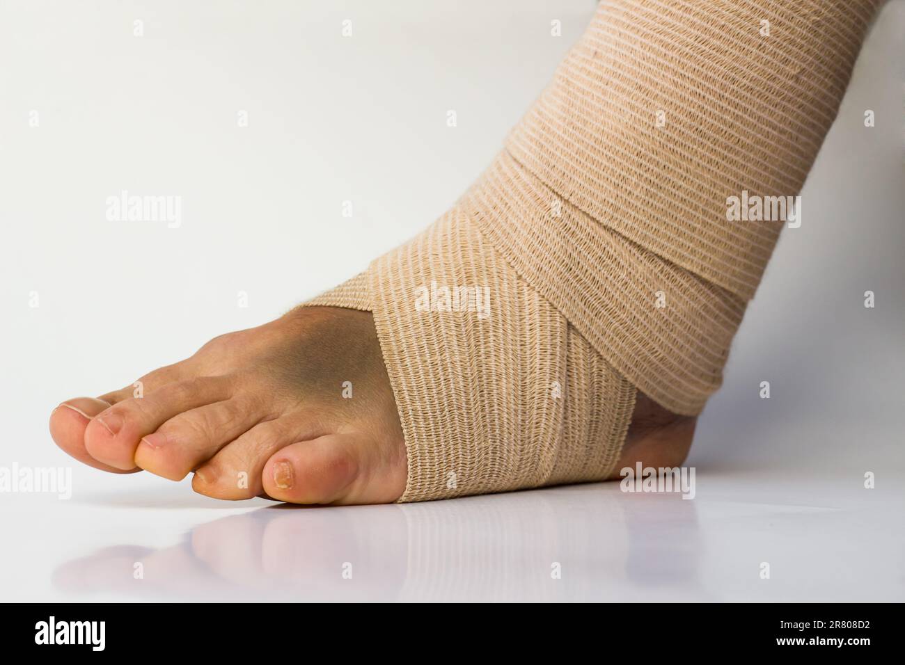 Medical bandage correctly wrapped around female sprained left ankle stand on white background with the reflection and copy space Stock Photo