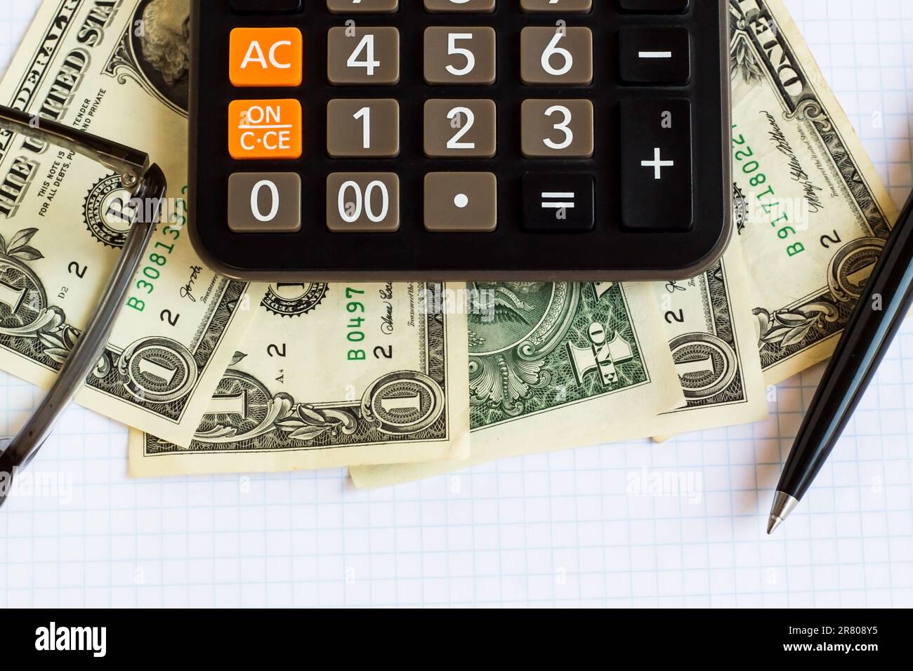 One US Dollar Bills on white checkered paper with calculator,pen and glasses.Conceptual image of finance Stock Photo
