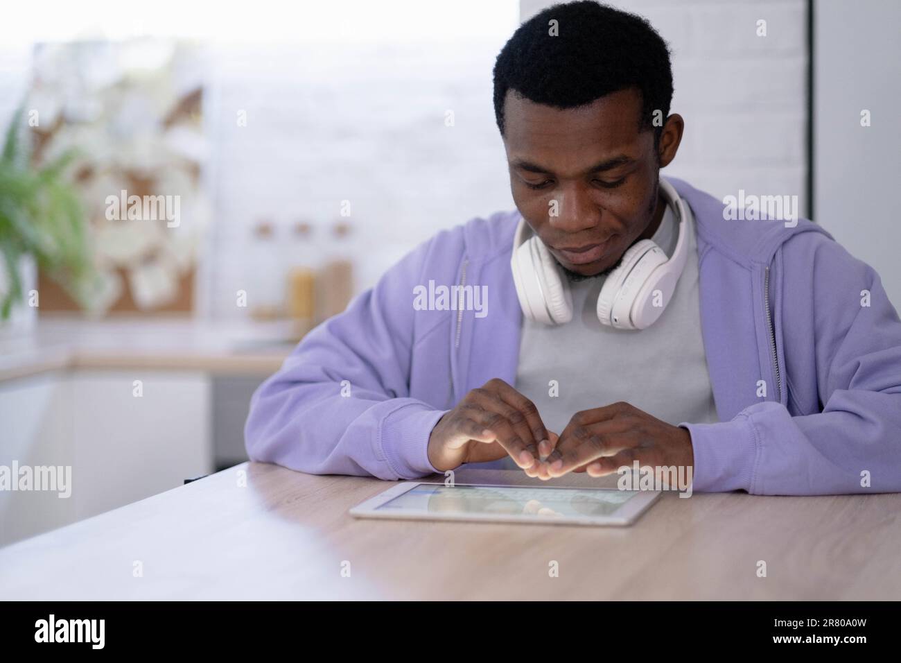 Black man using digital tablet on kitchen at home, working office work remotely typing text, African american freelancer using notepad computer Stock Photo
