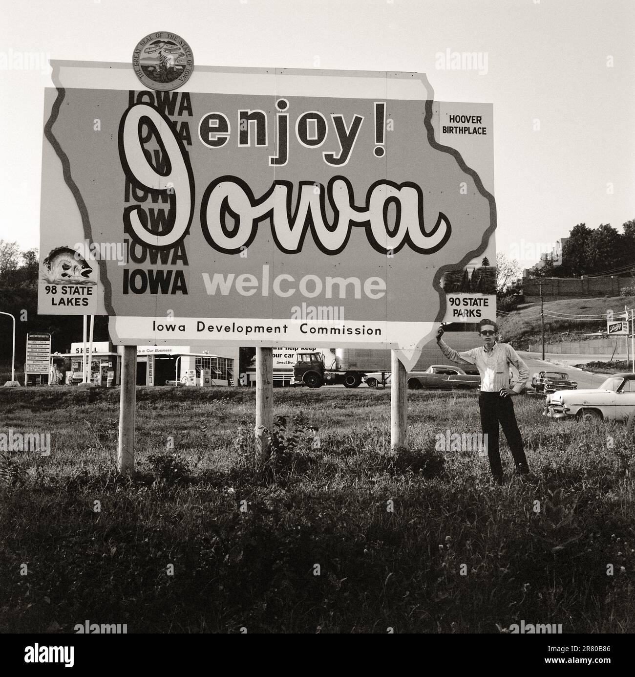 Iowa State Sign,1965. Man standing under Enjoy Iowa sign. Image