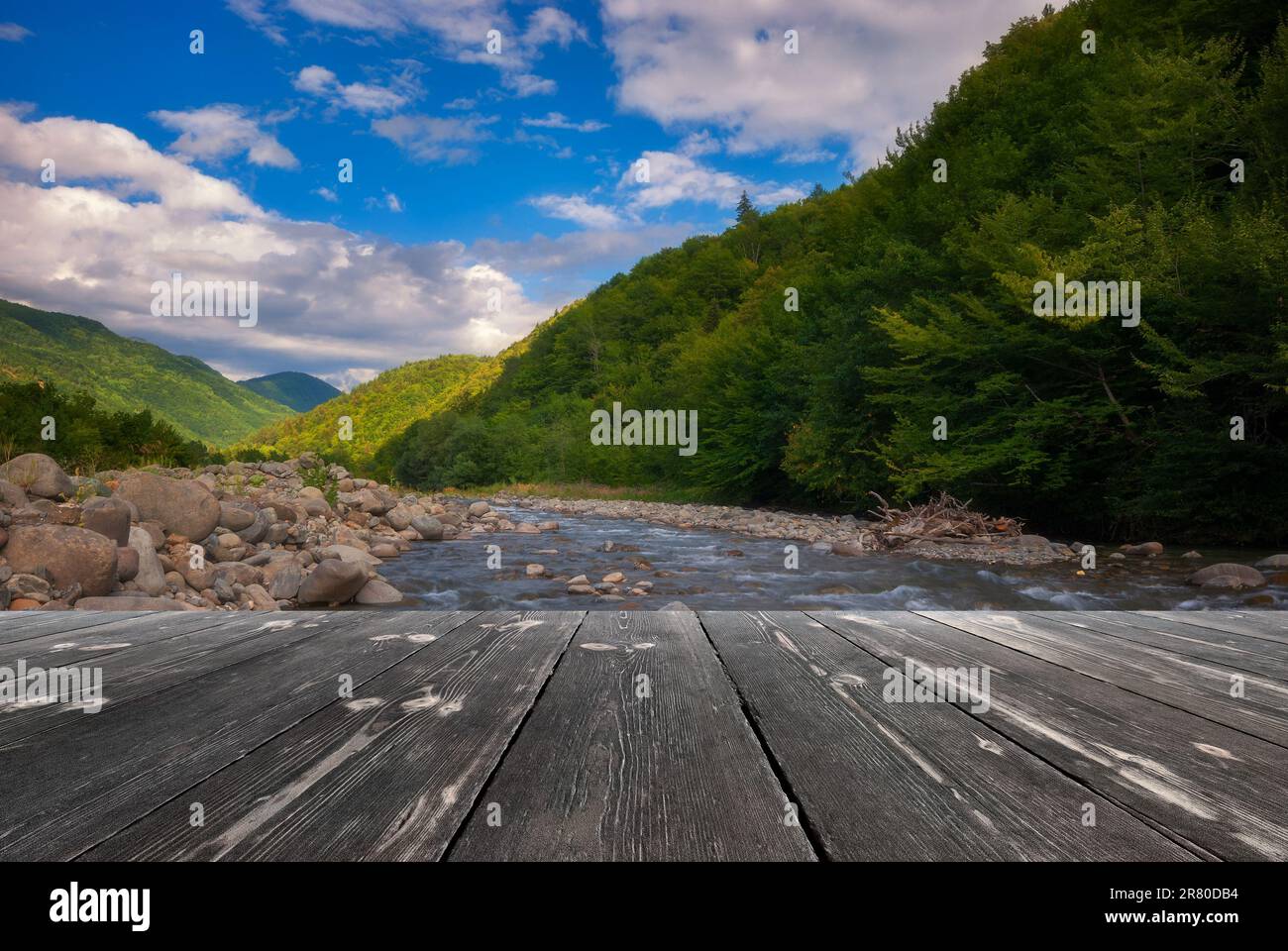Fast mountain river flowing with empty wooden batten bridge. Natural template landscape. Stock Photo