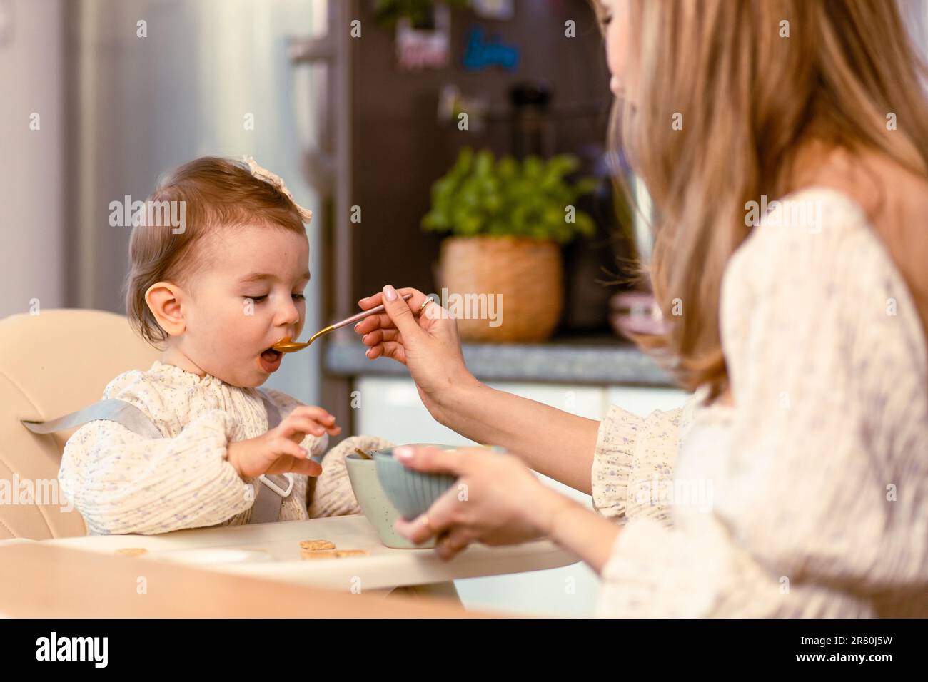 Young mom feeding her baby daughter with a spoon Stock Photo