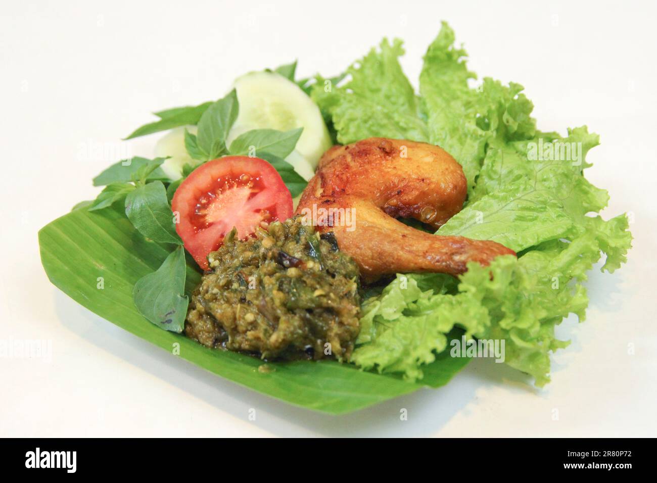 galangal fried chicken,sambal,tomato,cucumber,basil,lettuce.Indonesian food culinary on banana leaf plate.food art photography on white background Stock Photo