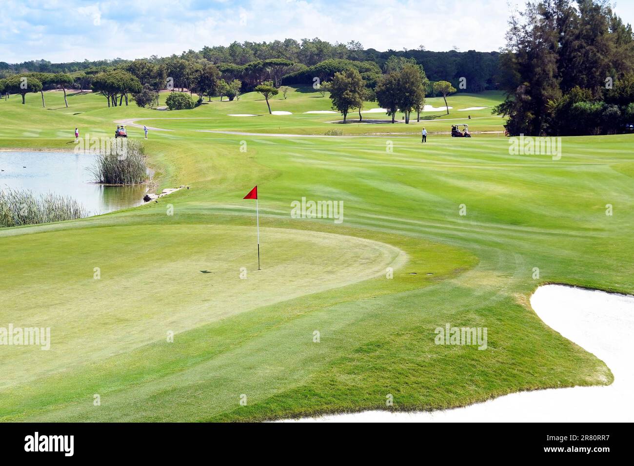 View across the 18th green and greenside bunker to the 18th fairway, around the water hazard, Laranjal Golf course, Algarve, Portugal. Stock Photo