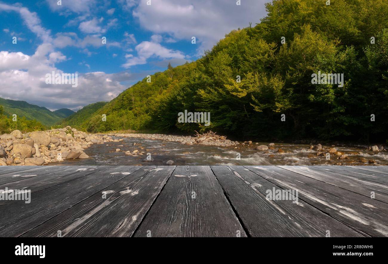 Fast mountain river flowing with empty wooden batten bridge. Natural template landscape. Stock Photo
