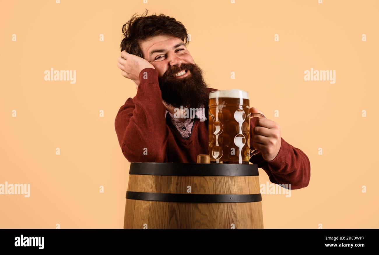 Smiling bearded man with mug of beer on wooden barrel. Celebration oktoberfest festival. Handsome man drinking draft beer at restaurant, pub or bar. M Stock Photo