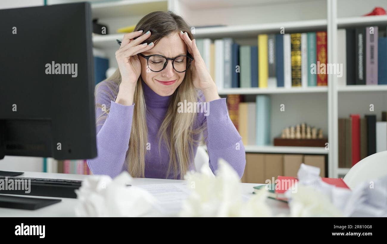 Young blonde woman student stressed sitting on table at library ...