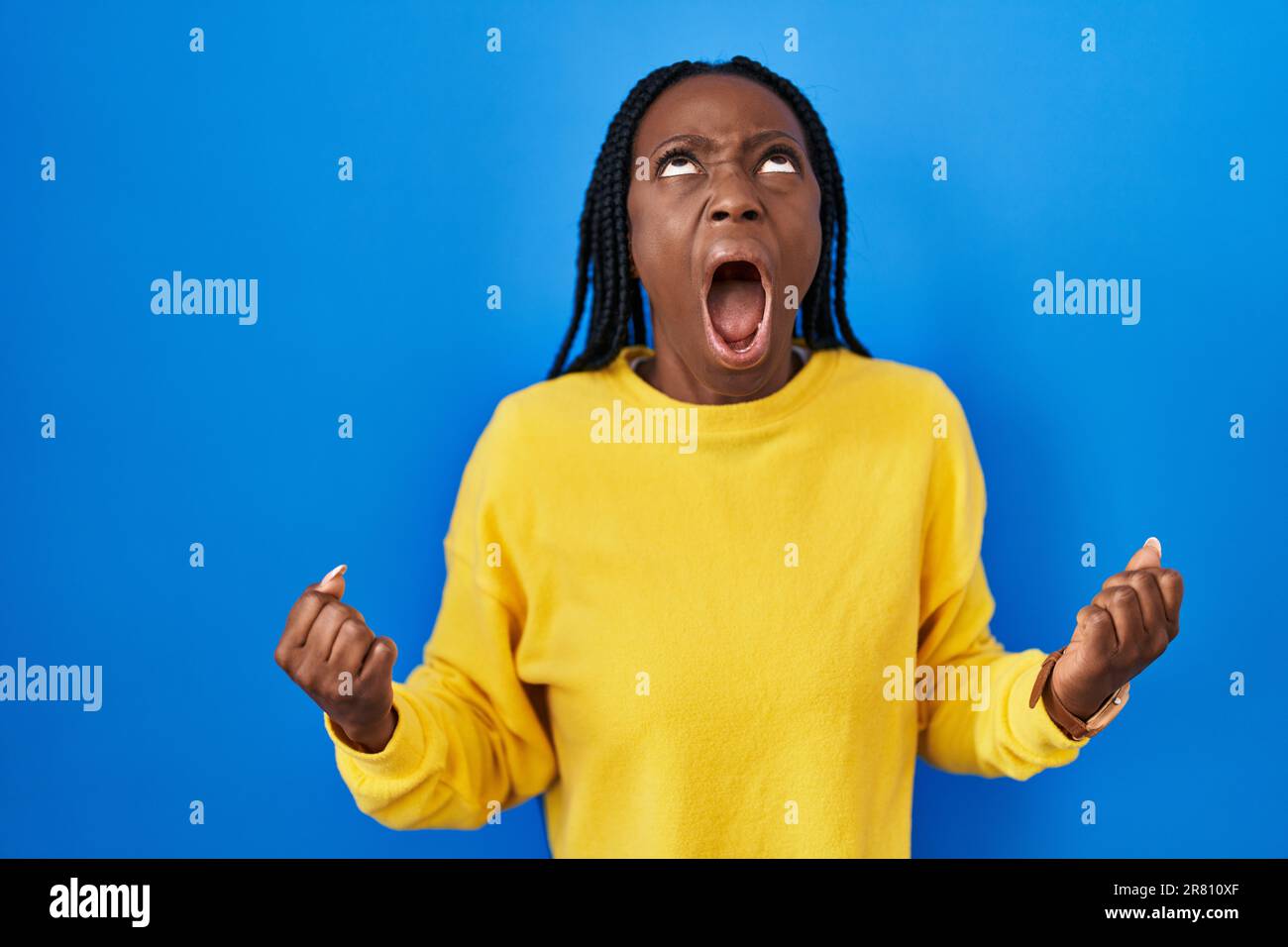 Beautiful black woman standing over blue background angry and mad ...