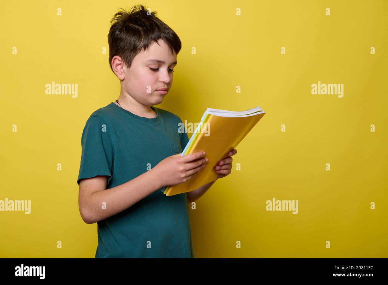 Adorable Caucasian schoolboy in green casual t-shirt, primary school student, holds colorful textbooks. Back to school. Stock Photo