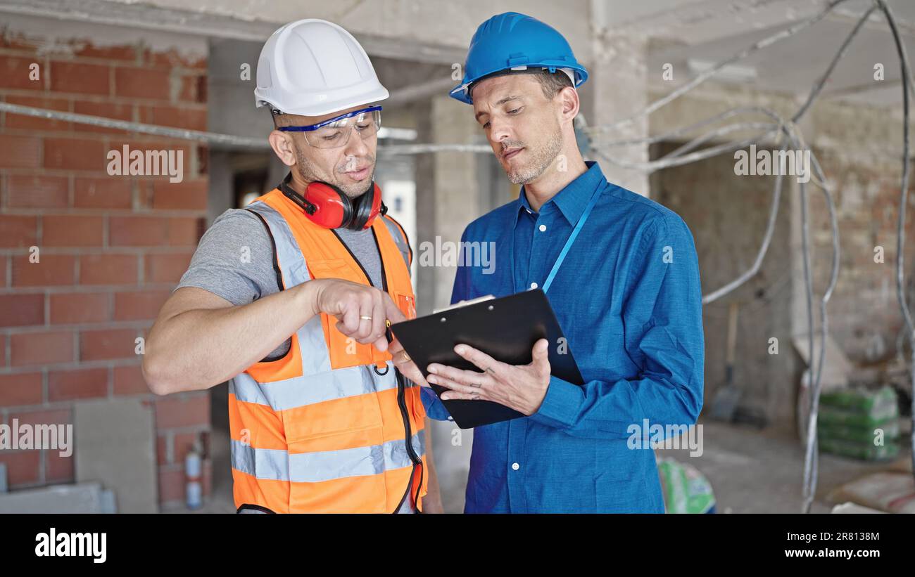 Two men builder and architect writing document speaking at construction ...