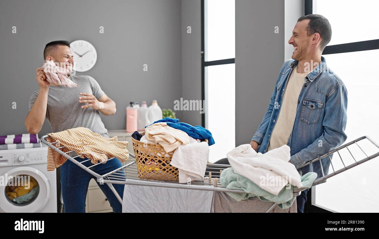 Two men couple doing laundry throwing clothes at laundry room Stock