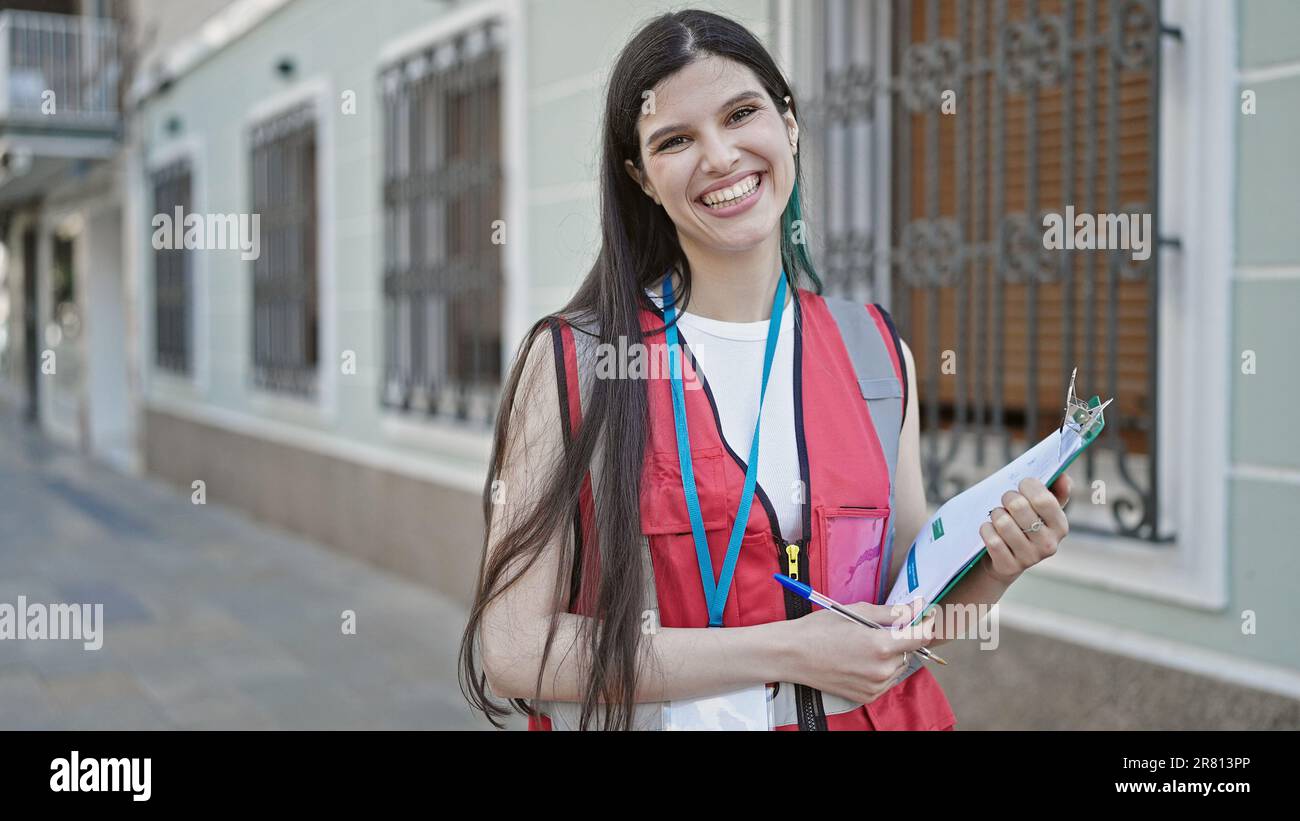 Young beautiful hispanic woman survey interviewer smiling confident holding clipboard at street Stock Photo