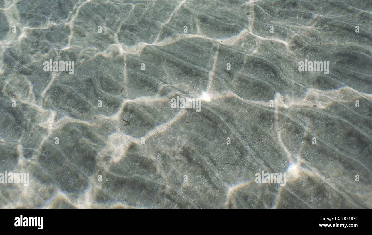 glare of sun plays on sandy bottom in shallow water. Top view on sandy seabed in shallow water with diagonal lines of sand and sun glare on its surfac Stock Photo