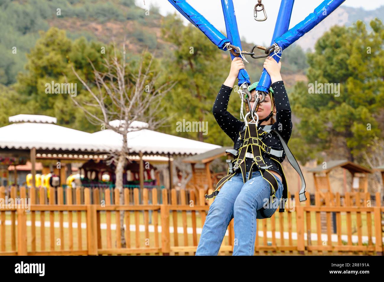 Teenage teen girl bungee flying in rope amusement park. Climbing harness equipment, green sports safety helmet. Hanging obstacle course. Kids children Stock Photo