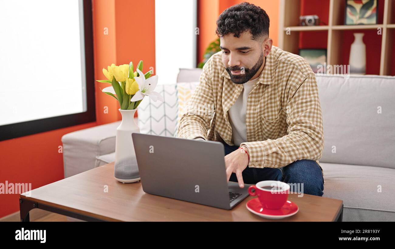 Young hispanic man using laptop drinking coffee at h Stock Photo