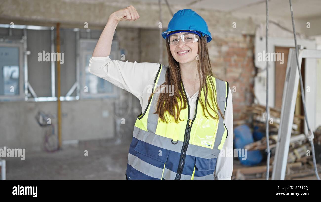 Young beautiful hispanic woman builder smiling confident doing strong gesture with arm at construction site Stock Photo