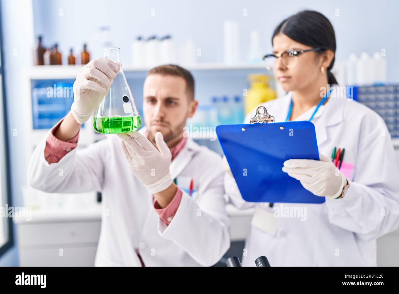Man and woman wearing scientists uniform measuring liquid at laboratory ...