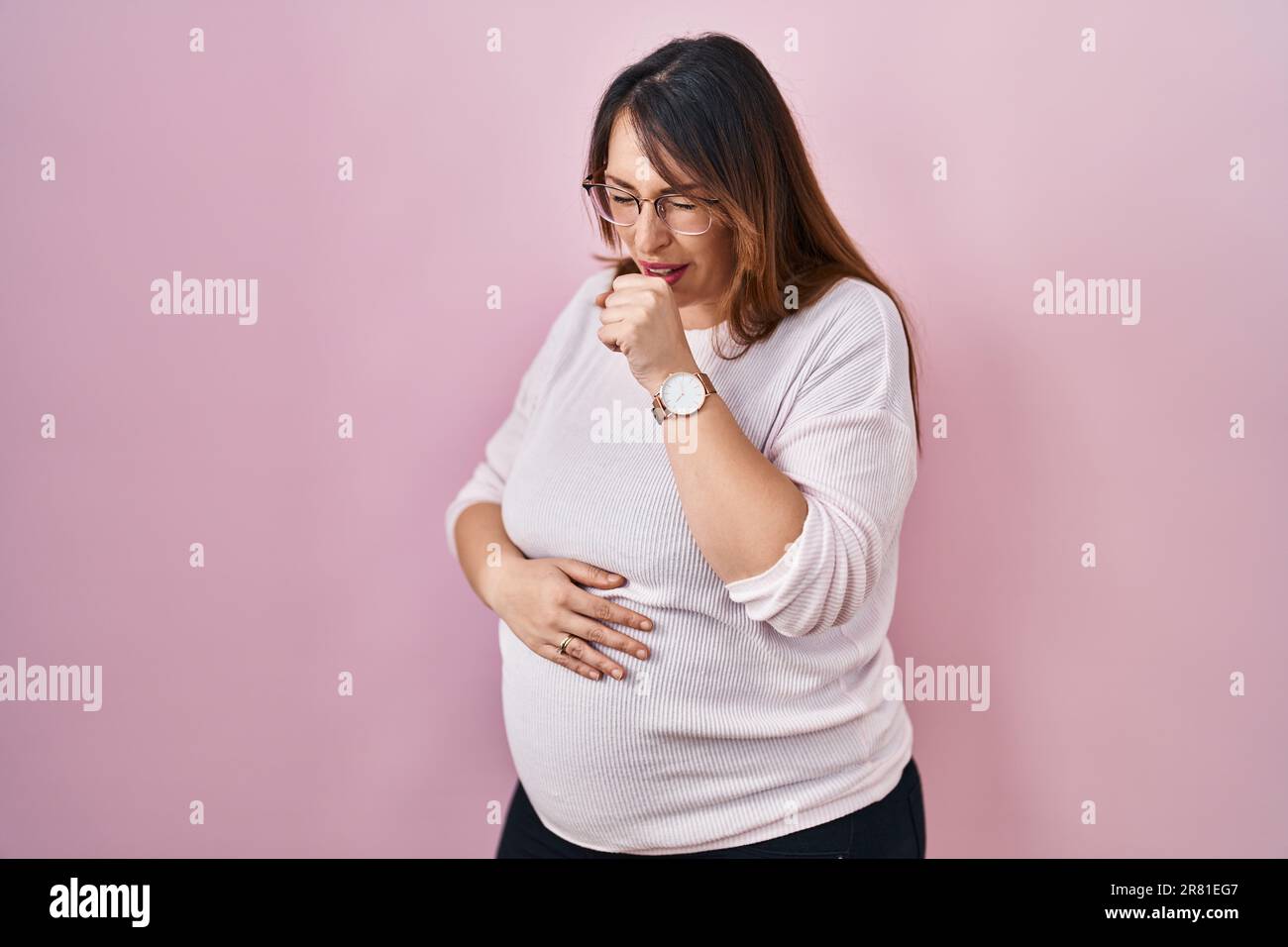 Pregnant woman standing over pink background feeling unwell and