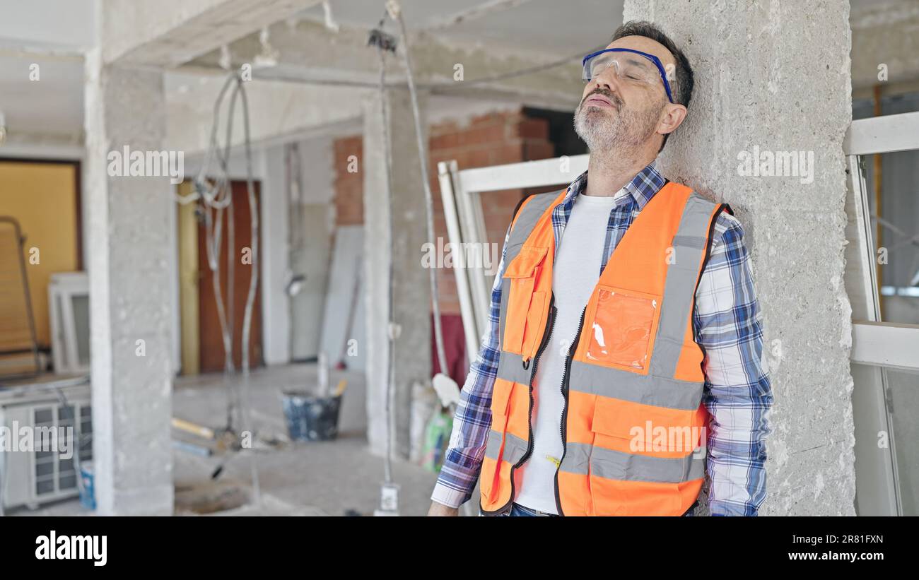 Middle age man builder tired taking out hardhat at construction site Stock Photo